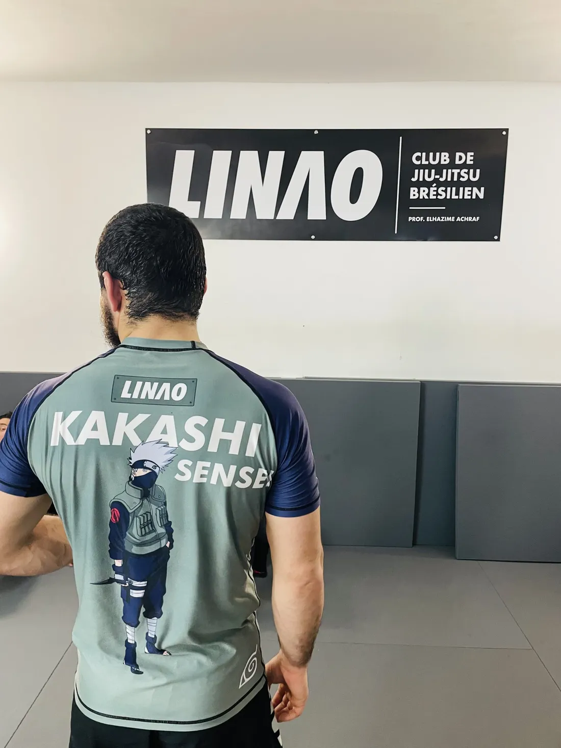 Rashguard LINAO personnalisé « Kakashi Sensei », porté de dos devant la bâche du club